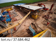 Uralsk region, Kazakhstan - May 24 2012: Oil deposit Zhaikmunai. Panorama of oil deposit and equipment of drilling rig. Pipes and machines. Engineer in orange work wear and white helmet. Редакционное фото, фотограф Alexey Rezvykh / Фотобанк Лори