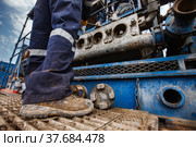 Uralsk region, Kazakhstan - May 24 2012: Oil deposit Zhaikmunai. Serviceman fixing mud pump engine. Baker Hughes company. Close-up of dirty working boots, no face. Редакционное фото, фотограф Alexey Rezvykh / Фотобанк Лори