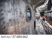 Ship-building plant. Scratched not painted metal cockpit with glass port-hole illuminator. Blured workers on background. (2012 год). Редакционное фото, фотограф Alexey Rezvykh / Фотобанк Лори