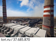 GRES-1 thermal power station. Grey raw coal bunkers on front. Smoke stacks both sides.Coal-harvesters in dust loading coal to electricity plant.Dry steppe,blue sky. Ekibastuz,Pavlodar reg.,Kazakhstan. Стоковое фото, фотограф Alexey Rezvykh / Фотобанк Лори