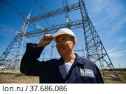 Ekibastuz, Kazakhstan - May 28 2012: Asian man engineer posing and smiling on Electric transformer and Distribution substation and Blue sky background. Редакционное фото, фотограф Alexey Rezvykh / Фотобанк Лори