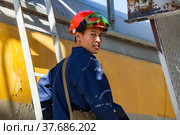 Caustic chemical plant. Young Asian worker in orange hardhat, green protective glasses and blue workwear posing and smiling on yellow railway tank wagon background (2012 год). Редакционное фото, фотограф Alexey Rezvykh / Фотобанк Лори