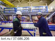 Pavlodar, Kazakhstan - May 29 2012: Caustic chemical plant. Chemical engineers in white hardhat and blue protective glasses discussing on electrolytic process machine background. Редакционное фото, фотограф Alexey Rezvykh / Фотобанк Лори