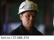 Aksu, Pavlodar region, Kazakhstan - May 29, 2012: Aksu steam power station. Portrait of adult Asian worker in white hardhat with respirator on. Close up photo. Blurred background. Редакционное фото, фотограф Alexey Rezvykh / Фотобанк Лори