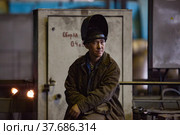 Aksu, Pavlodar region, Kazakhstan - May 29, 2012: Aksu steam power station. Asian welder resting in workshop. Protective mask open. Редакционное фото, фотограф Alexey Rezvykh / Фотобанк Лори