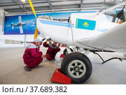 Karagandy, Kazakhstan - June 06, 2012: Aircraf-building plant KazAviaSpektr. Two workers makes service. National flag of Kazakhstan on cabin. Редакционное фото, фотограф Alexey Rezvykh / Фотобанк Лори