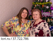 Радостные мама и дочка около новогодней елки в новогодние праздники. Joyful mom and daughter near the Christmas tree on New Year's holidays. (2022 год). Редакционное фото, фотограф Мария / Фотобанк Лори