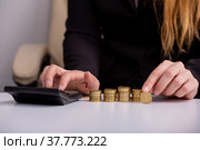 Бизнес леди считает на калькуляторе и держит монету в руке, за столом, перед стопками монет, крупным планом. Стоковое фото, фотограф Владимир Ходатаев / Фотобанк Лори