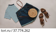 flat lay composition with female top, denim shorts, sandals and a wicker rattan bag on beige background top view. Стоковое фото, фотограф Galina kondratenko / Фотобанк Лори
