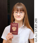 Девушка 14 лет с длинными светлыми волосами, в очках, белой блузке в черный горошек держит в руке свой первый российский паспорт. Стоковое фото, фотограф Цибаев Алексей / Фотобанк Лори