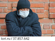 Мужчина в медицинской маске стоит на улице у кирпичной стены. Меры предосторожности при вирусной инфекции. Стоковое фото, фотограф Виталий Михайлюк / Фотобанк Лори