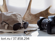 Солнцезащитные очки, шляпа от солнца и фотоаппарат лежат на белой глянцевой поверхности стола у окна. Стоковое фото, фотограф Борис Ряузов / Фотобанк Лори