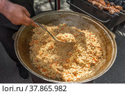 На уличном рынке продаются вкусный горячий плов и шашлык. Повар помешивает рис половником. Праздник сабантуй. Стоковое фото, фотограф Александр Бушков / Фотобанк Лори