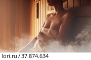 Young woman relaxing and sweating in hot sauna wrapped in towel. Girl In Sauna. Interior of Finnish sauna, classic wooden sauna with hot steam. Russian bathroom. Relax in hot sauna with steam. Стоковое фото, фотограф Сергей Тимофеев / Фотобанк Лори