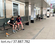 Подростки едят на автобусной остановке "Метро "Сухаревскя", Московский театр Олега Табакова" на Садовом кольце в Москве летом. Россия (2022 год). Редакционное фото, фотограф Овчинникова Ирина / Фотобанк Лори
