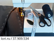 Sew at home. Processing the bottom of the  trousers on the sewing machine. Sewing accessories: black thread, needle threader, scissors and measuring tape. Стоковое фото, фотограф Виктория Катьянова / Фотобанк Лори