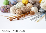 Accessories for hand knitting: metal, plastic and wooden knitting needles, hooks, balls of wool and acrylic yarn on a white background. Below is an empty space for text. Still life, closeup, copy space. Стоковое фото, фотограф Виктория Катьянова / Фотобанк Лори