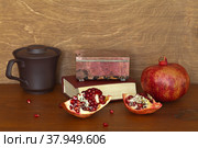Beautiful still life with ripe pomegranates, a rhodonite box on old book and a clay cup of garnet juice on wooden table. Front view, close-up. Стоковое фото, фотограф Виктория Катьянова / Фотобанк Лори