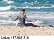 A surfer does a warm-up on the background of the sea on a sandy beach. Стоковое фото, фотограф Татьяна Дворецкая / Фотобанк Лори