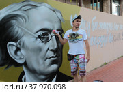Улыбчивы уличный художник Сергей Юраков расписывает стену центральной библиотеки имени Ф.И. Тютчева в Балашихе (2022 год). Редакционное фото, фотограф Дмитрий Неумоин / Фотобанк Лори
