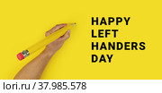 Left Hadnders day. Pencil in male left hand on yellow background. Стоковое фото, фотограф Kira_Yan / Фотобанк Лори