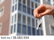Hand holds the keys to a new apartment on the background of the house. Housewarming and construction. Рука держит ключи от новой квартиры на фоне дома новостройки. Новоселье, ремонт и строительство. Стоковое фото, фотограф Aleksandra Selivanova / Фотобанк Лори