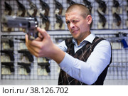 Interested man imitating aiming with pistol in gun shop. Стоковое фото, фотограф Яков Филимонов / Фотобанк Лори