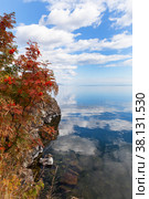 Picturesque autumn landscape of Lake Baikal and Cape Shamansky. Red rowan bushes on the rocky shore of the cape. Clouds are reflected in calm water. Natural background. Autumn travel and outdoors. Стоковое фото, фотограф Виктория Катьянова / Фотобанк Лори