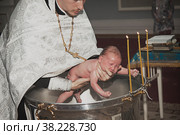 Infant baptism in Orthodox Church. Priest holds newborn child in his arms at baptismal font with Holy water. Baby is bathed in water. Sacrament rite of baptism (2016 год). Редакционное фото, фотограф Aleksandr Golubev / Фотобанк Лори