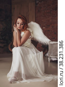 Pretty slender woman with wings. Female in stage image of an angel. Emotion girl in dress sitting on chair in an old textured room. Actress shows abilities. Concept of theatrical premiere. Copy space. Стоковое фото, фотограф Aleksandr Golubev / Фотобанк Лори