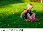 Cute little blond baby girl two year old playing with teddy bear on fresh green grass with flowers. Kid having fun making first steps on mowed natural lawn. Happy and healthy childhood concept. Стоковое фото, фотограф Aleksandr Golubev / Фотобанк Лори