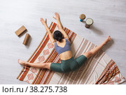 Молодая женщина в спортивной одежде, занимающаяся йогой, выполняет упражнение самоканасана, сидя на одеяле в поперечном шпагате с наклоном тела вперед. Стоковое фото, фотограф Сергей Чайко / Фотобанк Лори