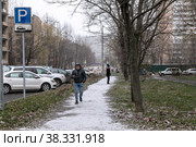 Москва, ноябрь. Выпал первый снег и побелил дорожку на зеленом травяном газоне. По снежной дороге идет мужчина (2022 год). Редакционное фото, фотограф Наталья Николаева / Фотобанк Лори