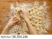 Две детские руки отрывают кусочек теста на фоне скатанных шариков лежащих на деревянном столе осыпанном мукой. Крупный план. Вид сверху. Стоковое фото, фотограф Диана Гарифуллина / Фотобанк Лори