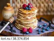 Delicious pancakes with honey, blueberries and raspberries. Next to it is a wooden barrel with an inscription in Russian: "honey". The concept of the Maslenitsa holiday. Стоковое фото, фотограф Photojuli / Фотобанк Лори