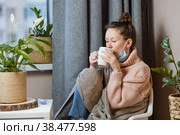 Больная привлекательная молодая женщина простужена и пьет горячий чай, расстроенная молодая блондинка в свитере и одеяле чувствует себя плохо, надевает медицинскую маску. Простуда, высокая температура, грипп, озноб. Стоковое фото, фотограф Photojuli / Фотобанк Лори