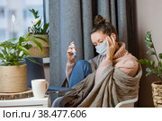 Больная европейская привлекательная молодая женщина простудилась и смотрит на градусник Расстроенная молодая блондинка в свитере и одеяле чувствует себя плохо, надевает медицинскую маску. Озноб, болезнь, высокая температура. Стоковое фото, фотограф Photojuli / Фотобанк Лори