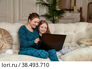 Smiling mother and teen girl daughter watching happy movie on laptop on sofa in living room at home. Concept of spending time together with kids and family lovely relationships. Copy text space. Стоковое фото, фотограф Aleksandr Golubev / Фотобанк Лори