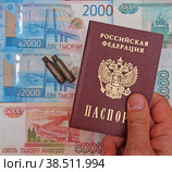 Мужская рука держит российский паспорт на фоне из рублевых купюр и гильз от патронов. Стоковое фото, фотограф Цибаев Алексей / Фотобанк Лори
