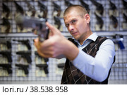 Interested man imitating aiming with pistol in gun shop. Стоковое фото, фотограф Яков Филимонов / Фотобанк Лори