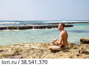 Bearded young man drummer, playing rhythm with djembe drum, sitting on tropical coral reef coast at ocean background. Travel vacation and music relaxation concept. Selective focus. Copy text space. Стоковое фото, фотограф Aleksandr Golubev / Фотобанк Лори