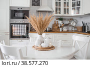 Still-life. Dried pampas grass in a vase, white ceramic pumpkins, a teapot and pumpkin-shaped candles on a white table in the interior of a Scandinavian-style home kitchen. Cozy autumn concept. Стоковое фото, фотограф Photojuli / Фотобанк Лори