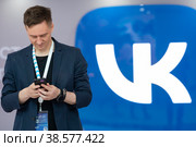 Россия. Санкт-Петербург. Молодые люди со смартфоном на фоне логотипа социальной сети ВКонтакте. Russia. Saint-Petersburg. Young people with a smartphone on the background of the VKontakte social network logo. (2022 год). Редакционное фото, фотограф Алексей Смышляев / Фотобанк Лори