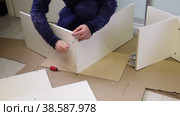The man connects the side panel and the cover with a Euro screw. Wooden modular rack. Assembling a modular rack. Overall plan. Стоковое видео, видеограф Vadzim Yakubovich / Фотобанк Лори