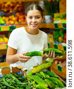 Portrait of young female choosing fresh bitter melon (Momordica charantia) in store. Стоковое фото, фотограф Яков Филимонов / Фотобанк Лори