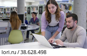 Emotional student girl, preparing for classes on a laptop with a guy classmate in the university library, points him to something in the monitor. Стоковое видео, видеограф Яков Филимонов / Фотобанк Лори