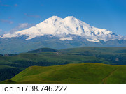 Nature mountain range. Amazing perspective of caucasian snow mountain or sleeping volcano Elbrus with green fields, blue sky background. White Elbrus landscape view - highest peak of Russia and Europe. Стоковое фото, фотограф Евгений / Фотобанк Лори