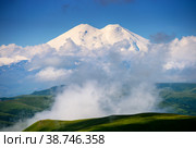 Great nature mountain range. Amazing perspective of caucasian snow mountain or volcano Elbrus with cloudy green field, blue sky background. Elbrus landscape view - highest peak of Russia and Europe (2018 год). Редакционное фото, фотограф Евгений / Фотобанк Лори