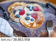 Delicious pancakes with honey, blueberries and raspberries. Next to it is a wooden barrel with an inscription in Russian: "honey". The concept of the Maslenitsa holiday. Стоковое фото, фотограф Photojuli / Фотобанк Лори