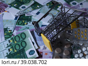 medicines and pills are lying in a small shopping cart against the background of money euro dollars 100 500. pills are poured out of the cart for money the problem of the cost of medicines expensive m. Стоковое фото, фотограф Meshkov Sergey / Фотобанк Лори